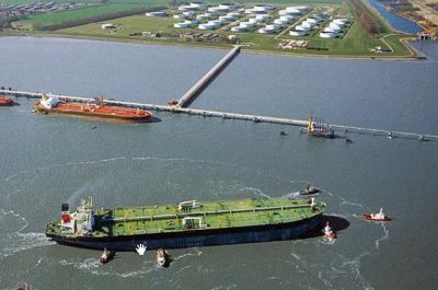 Luftbildaufnahme der Tankerlöschbrücke im Vordergrund. Am oberen Bildrand ist das Festland mit zahlreichen weißen Tanks zu erkennen. 